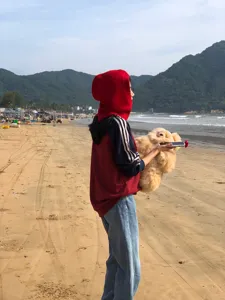 Vue détaillée d'un bonnet cagoule en laine rouge unie porté en extérieur sur une plage.