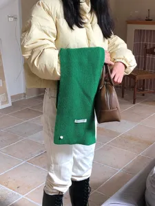 Nahaufnahme des grünen Strickschals mit weicher Wollmischung Textur und Markenetikett.