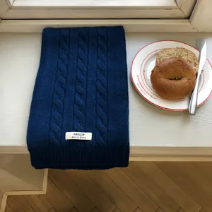 Detailansicht des dunkelblauen Zopfmuster Strickschals auf der weißen Fensterbank im Winter.