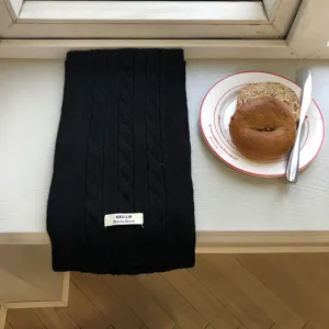 Detailansicht eines schwarzen Strick-Winterschals, flach auf weißem Untergrund liegend.