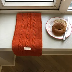 Detailansicht des gemütlichen orangen Zopfmuster-Winterschals auf heller Fensterbank.