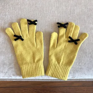 Detailaufnahme gelber Strickhandschuhe mit süßen schwarzen Samtschleifen an den Fingern, cozy.