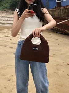 Detailaufnahme einer stilvollen braunen Strick-Handtasche im Strand-Szenario präsentiert.