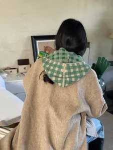 Detail view of the green white plaid knitted hooded shawl with beige coat for winter style.