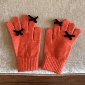 Nahaufnahme oranger Strickhandschuhe mit schicken schwarzen Schleifen an den Fingern.