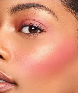 Close-up beauty shot showing makeup application with vibrant blush and striking blue mascara.