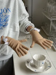 Detailansicht winterlicher, camelbrauner Strickhandschuhe mit niedlichen weißen Bommeln.