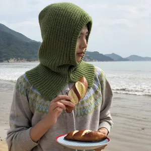 Close-up view of the knitted balaclava hood and scarf combo worn by model at beach.