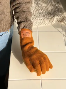 Detailaufnahme von warmen Strickhandschuhen in Karamell mit Etikett auf Fliesenoberfläche