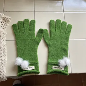Detailansicht winterlicher grüner Strickhandschuhe mit weißen Bommeln und gerippten Bündchen.