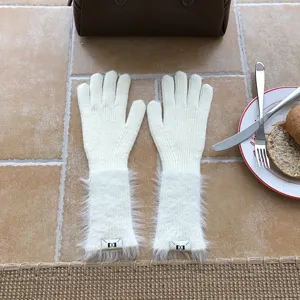 Nahaufnahme eleganter cremeweisser Strickhandschuhe mit flauschigen Bündchen und kleinen Labeln.