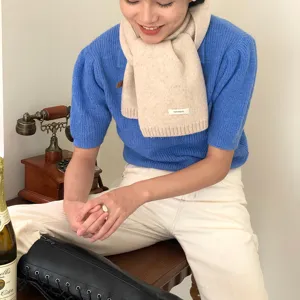 Detailaufnahme des gemütlichen, beige gestrickten Winterschals mit Wolletikett im Szenenbild.
