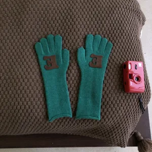 Detailaufnahme grüner Strickhandschuhe mit braunem Buchstabenaufnäher für Herbst Winter.