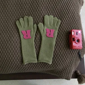 Detailansicht grüner Strickhandschuhe mit rosa R-Aufnäher für kuschelige Wintertage.