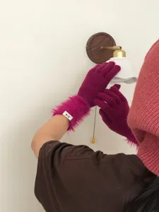 Detailaufnahme magentaroter Strickhandschuhe mit Plüschbündchen an einer modernen Wandlampe.