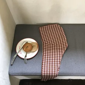 Detailed shot of a brown and pink houndstooth knit balaclava scarf styled on a cozy grey bench.