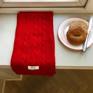 Detailansicht eines weichen roten Zopfmuster-Winterschals auf einer weißen Fensterbank.