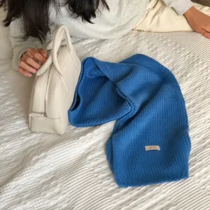 Naheaufnahme der kuscheligen blauen Strickschal Textur und des Etiketts auf weißem Bett.