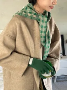Detail view of stylish autumn winter plaid scarf and green knit gloves matching cozy beige coat.