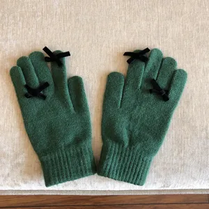 Grüne Strickhandschuhe mit schwarzen Schleifen, warmes Wollmaterial, touchscreenfähig.