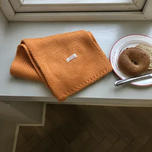 Detaillierte Nahaufnahme eines kuscheligen orangefarbenen Strickschals auf der Fensterbank.