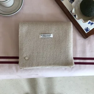 Nahaufnahme der weichen, beigen Strickschaltextur, ordentlich gefaltet mit eleganten Requisiten.