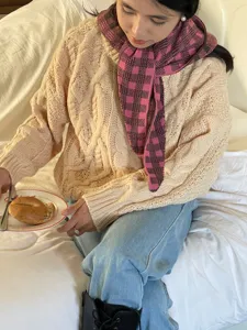 Detailed view of the cozy beige cable knit sweater and stylish pink plaid scarf outfit.