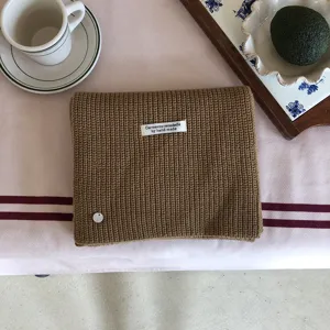 Nahaufnahme der braunen Strickschal-Textur mit handgefertigtem Etikett und gemütlichem Styling.