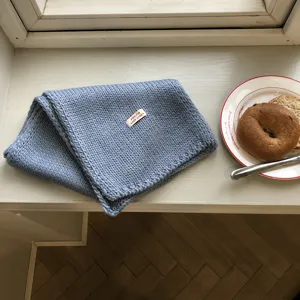 Detailansicht eines weichen blauen Strickschals mit grober Textur und handgefertigtem Etikett.