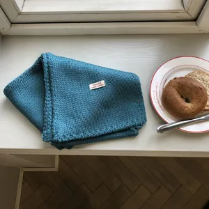 Gemütlicher blauer Strickschal Detailansicht am sonnigen Fensterbrett, weiche Wolle, warmer Stil.