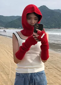 Red knitted arm warmers and matching hood set detail shot on beach background for winter.