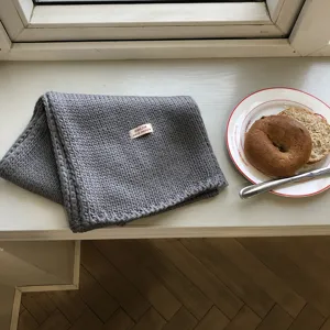 Detailansicht des gemütlichen grauen Strickschals auf der Fensterbank mit Lifestyle-Requisite.