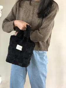 Detail view of the black plush checkered handbag, showing soft faux fur and woven texture.