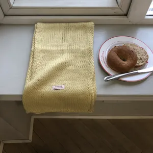 Detailaufnahme eines weichen Strickschals auf einer gemütlichen Fensterbank mit Brot.