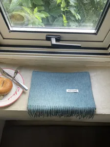 Detail view of solid blue winter wool scarf with tassel ends and 100% wool label on windowsill.
