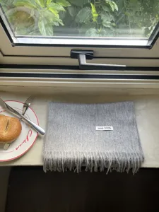 Detail shot of grey wool scarf fringe and 100% wool label on natural windowsill.