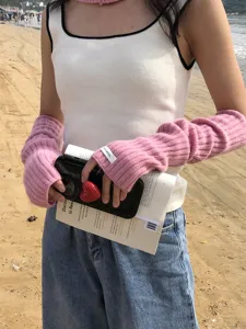 Close-up detail of cozy pink knitted arm warmers worn at the beach. Soft wool winter sleeve.