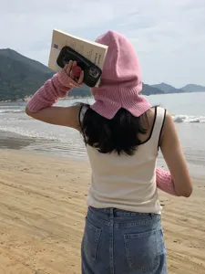 Detail view of women pink knitted balaclava hood and long arm warmers on beach background.