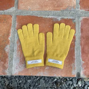 Nahaufnahme von einfarbigen gelben Strick-Touchscreen-Handschuhen mit Markenetikett am Bündchen.