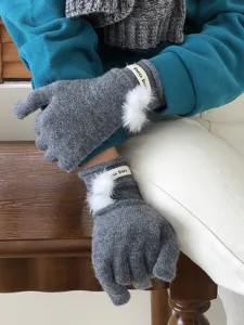 Detailansicht winterwarmer grauer Strickhandschuhe mit süßen weißen Bommeln für Damen.