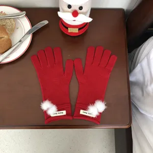 Detailansicht roter Winter-Strickhandschuhe mit weißen Plüschbällen und Markenschild.