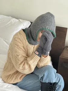 Cozy grey knitted balaclava with green trim detail and matching fuzzy gloves set in bedroom lifestyle view