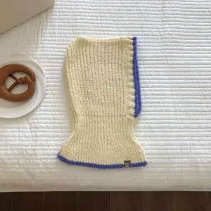 Close-up detail of knitted balaclava in cream and purple contrast trim, cozy winter flat lay.