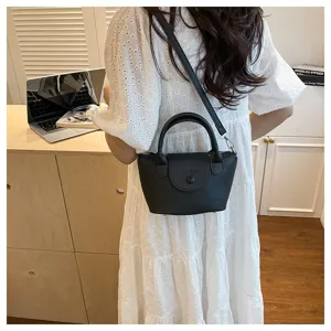 Detailed view of black textured leather top handle crossbody bag worn with white dress.