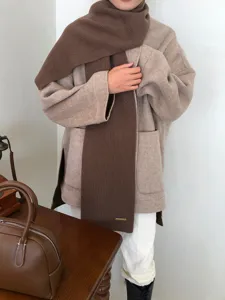 Nahaufnahme eines kuscheligen braunen Strickschals kombiniert mit einem eleganten Mantel.
