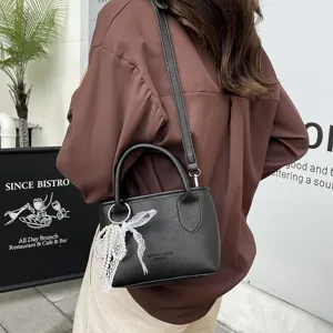 Detail shot of black faux leather crossbody handbag featuring elegant pearl and lace charm pendant.