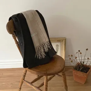 Detailansicht eines klassischen Wollschals mit Karomuster auf einem alten Holzstuhl.