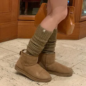 Detailopname van bruine gebreide wollen beenwarmers gecombineerd met korte laarzen in de herfst.