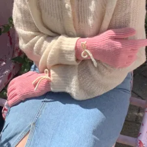 Close-up detail of cozy pink knit gloves featuring cute white bow accents on the wrist.
