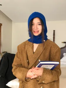 Detailed shot of a cozy blue knitted balaclava hood scarf worn in a warm room setting.
